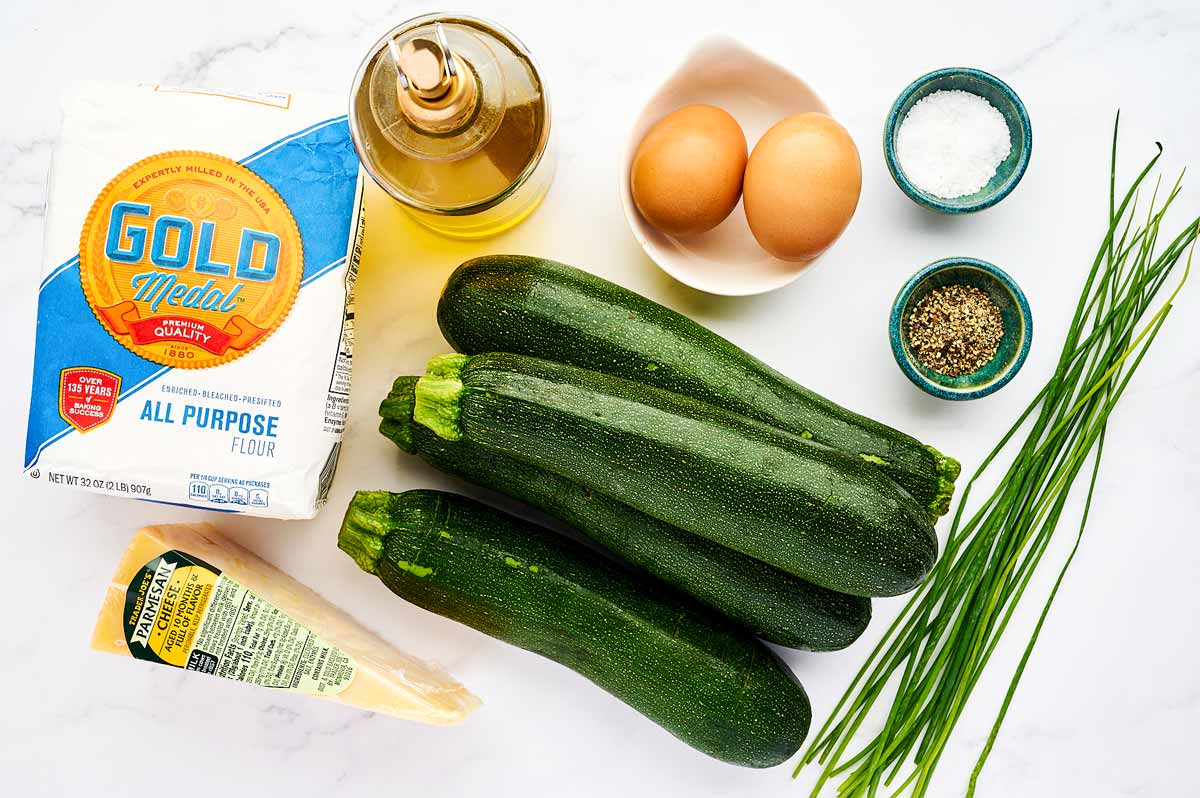 Ingredients for zucchini fritters on a white marble surface.