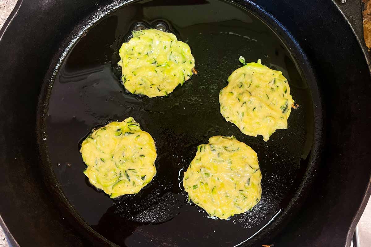 Uncooked zucchini fritters in a skillet.