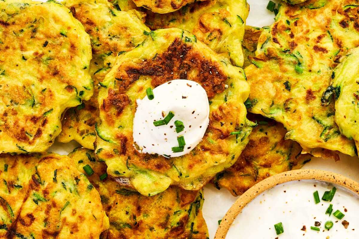 Overhead view of zucchini fritters with sour cream.