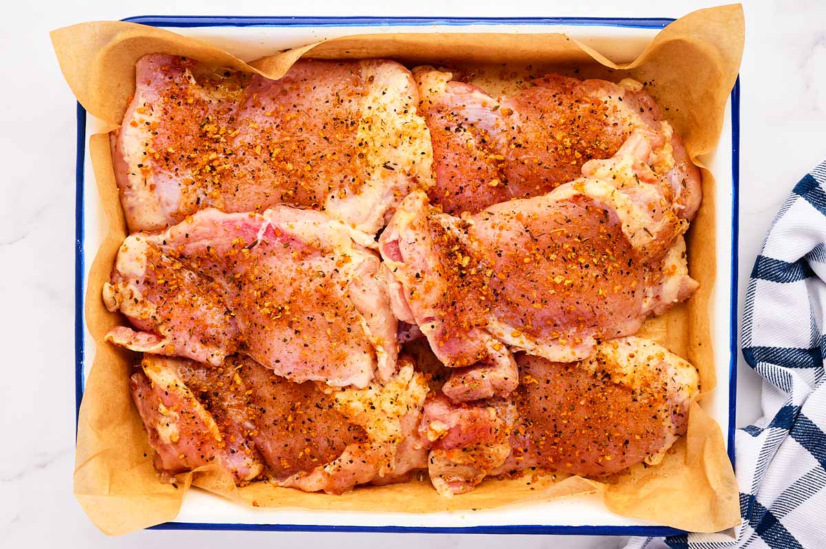 Seasoned chicken thighs in a pan.