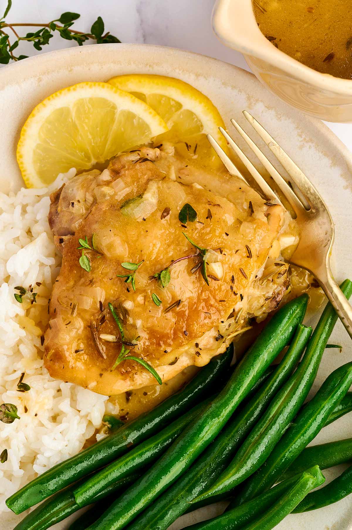 Lemon chicken thigh on plate with rice and green beans.
