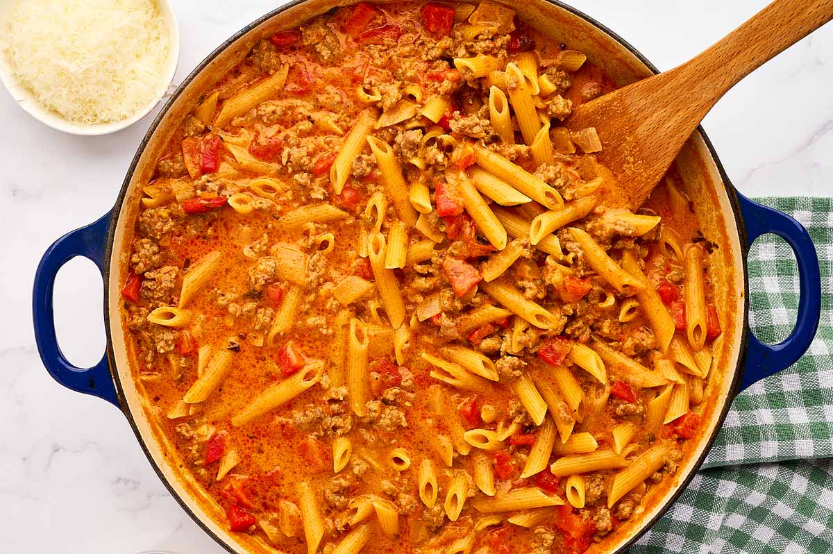 Cooked sausage and peppers pasta in pan with a wooden spatula.