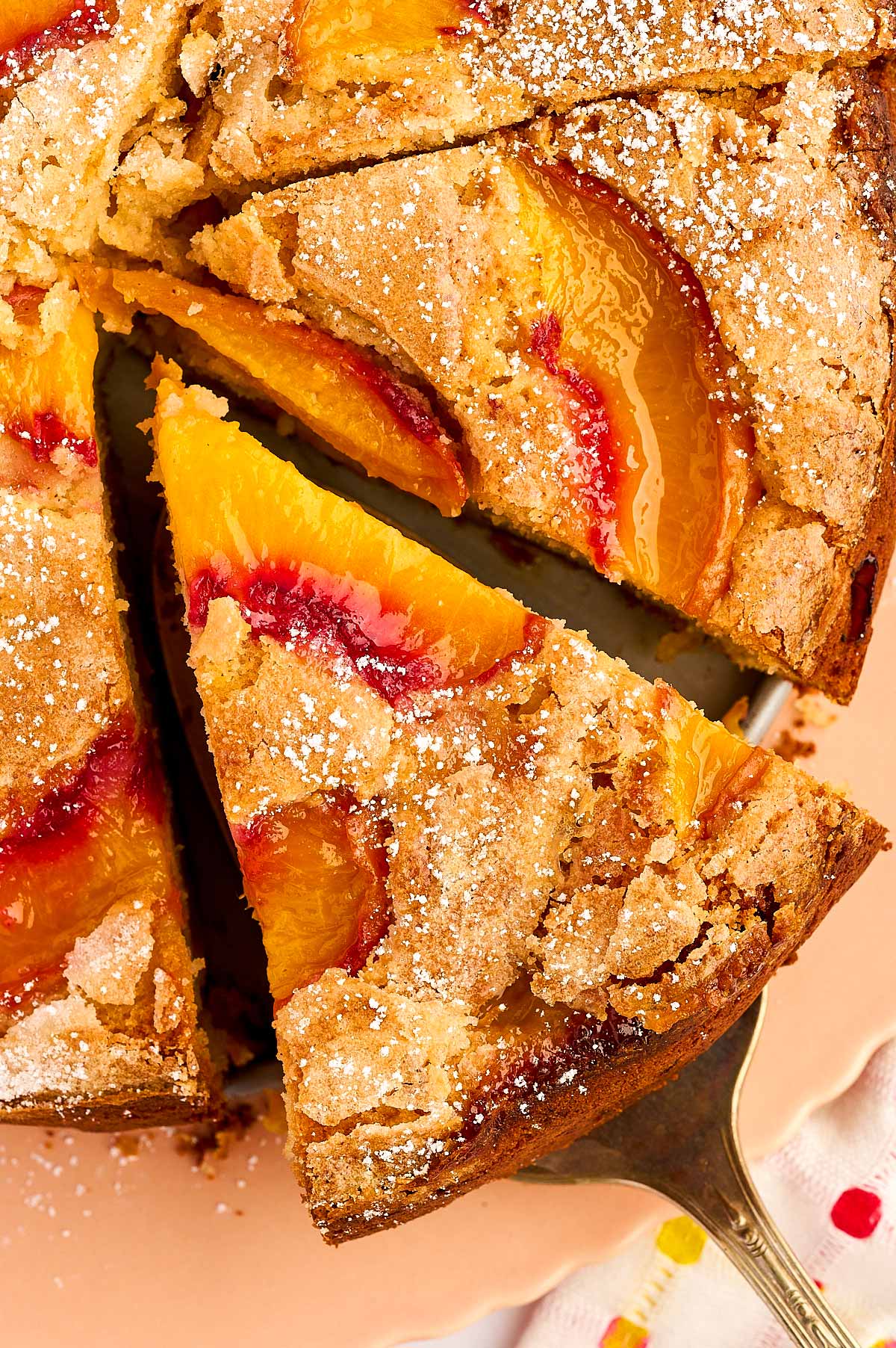 Slice of peach cake being taken from a whole cake.