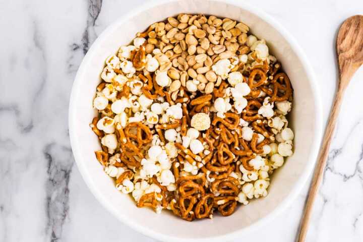 Popped popcorn, pretzels and roasted peanuts in a white bowl.