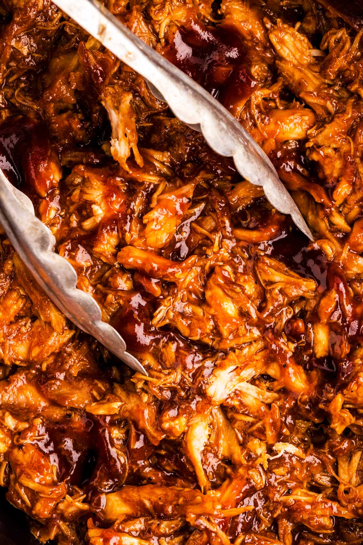 Close up photo of metal tongs in bbq chicken.