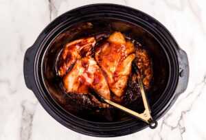 Raw chicken in slow cooker with bbq sauce.