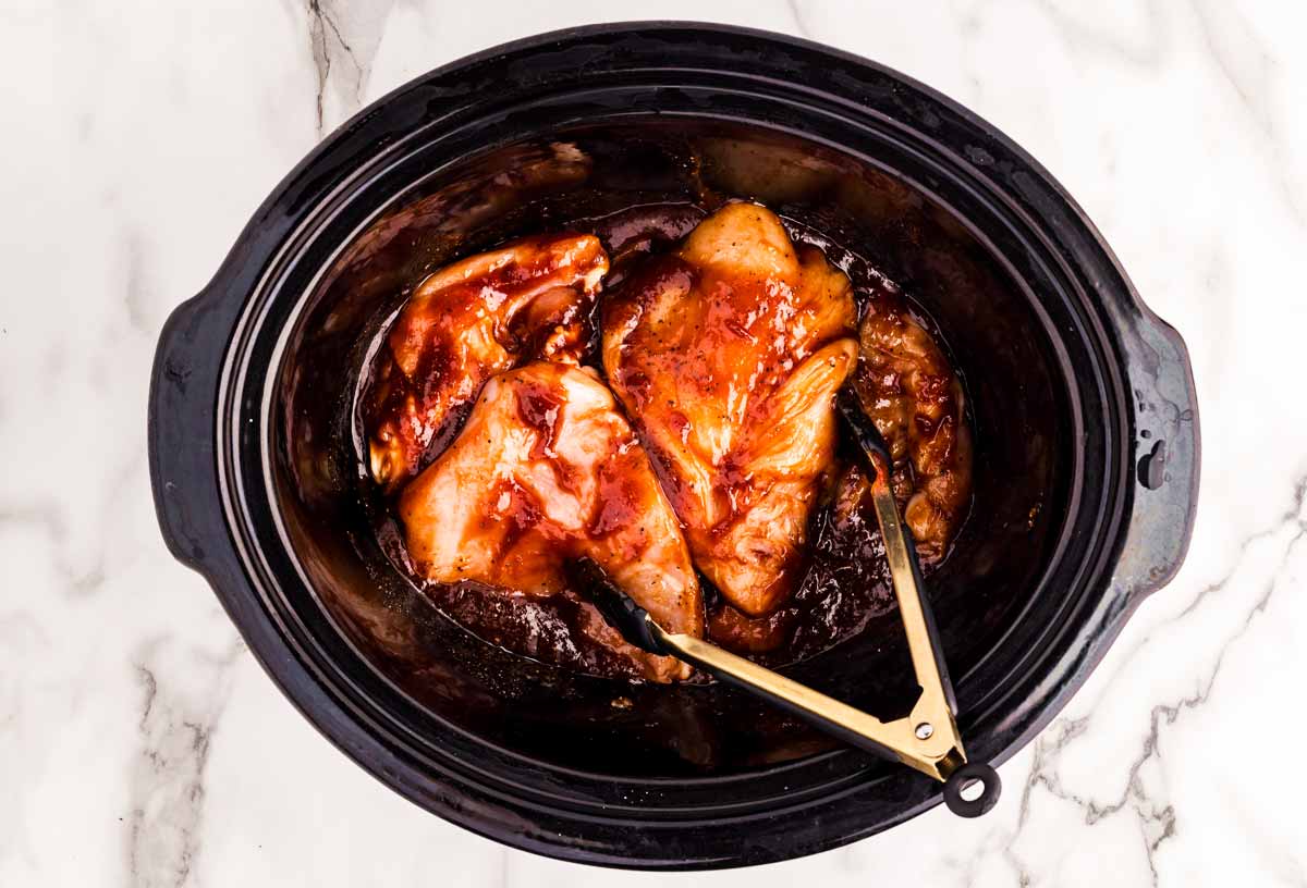 Raw chicken in slow cooker with bbq sauce.