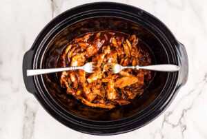 Shredding chicken in bbq sauce in a slow cooker with two forks.