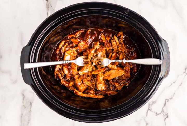 Shredding chicken in bbq sauce in a slow cooker with two forks.