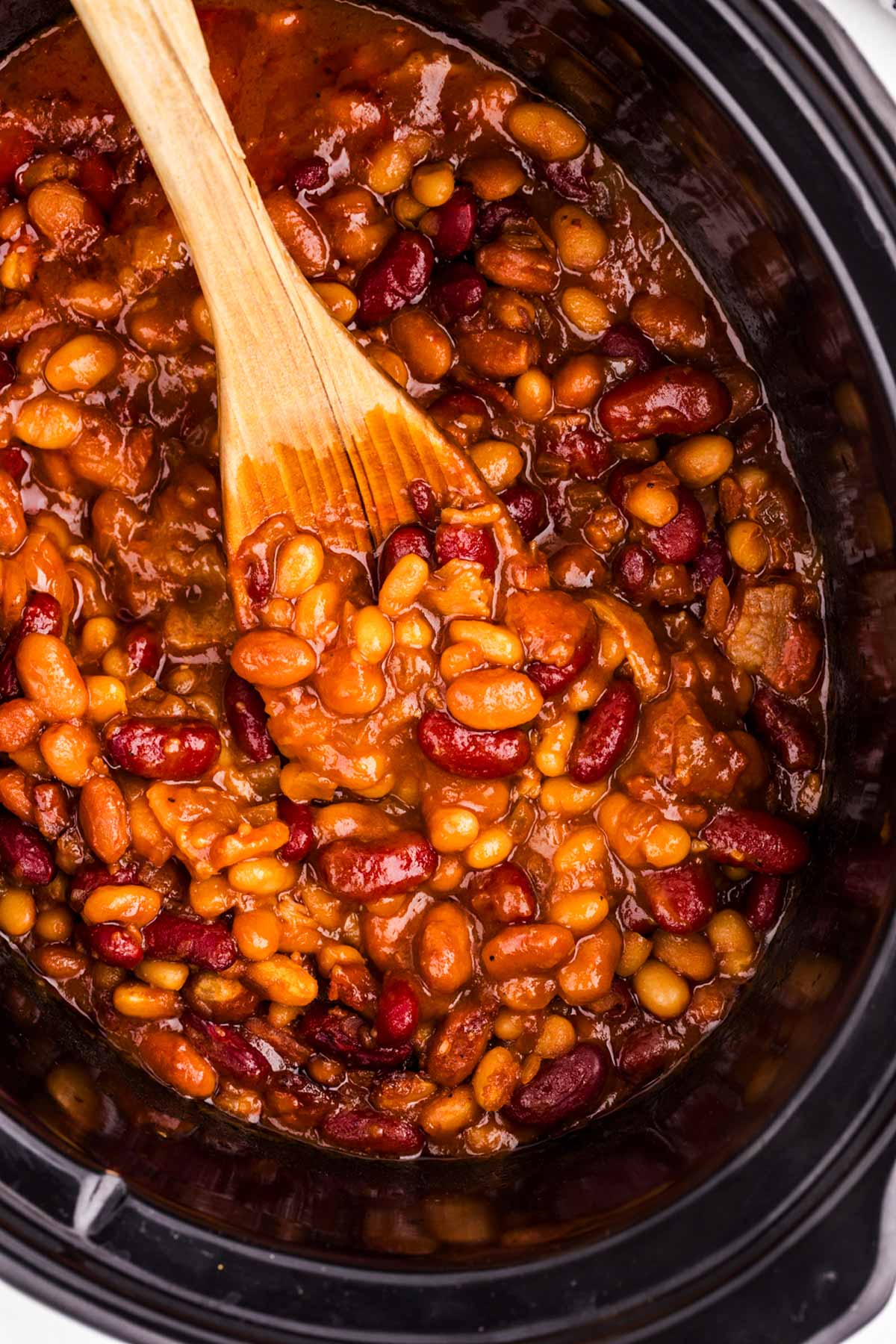 Overhead view of a wooden spoon in a crockpot full of baked beans.