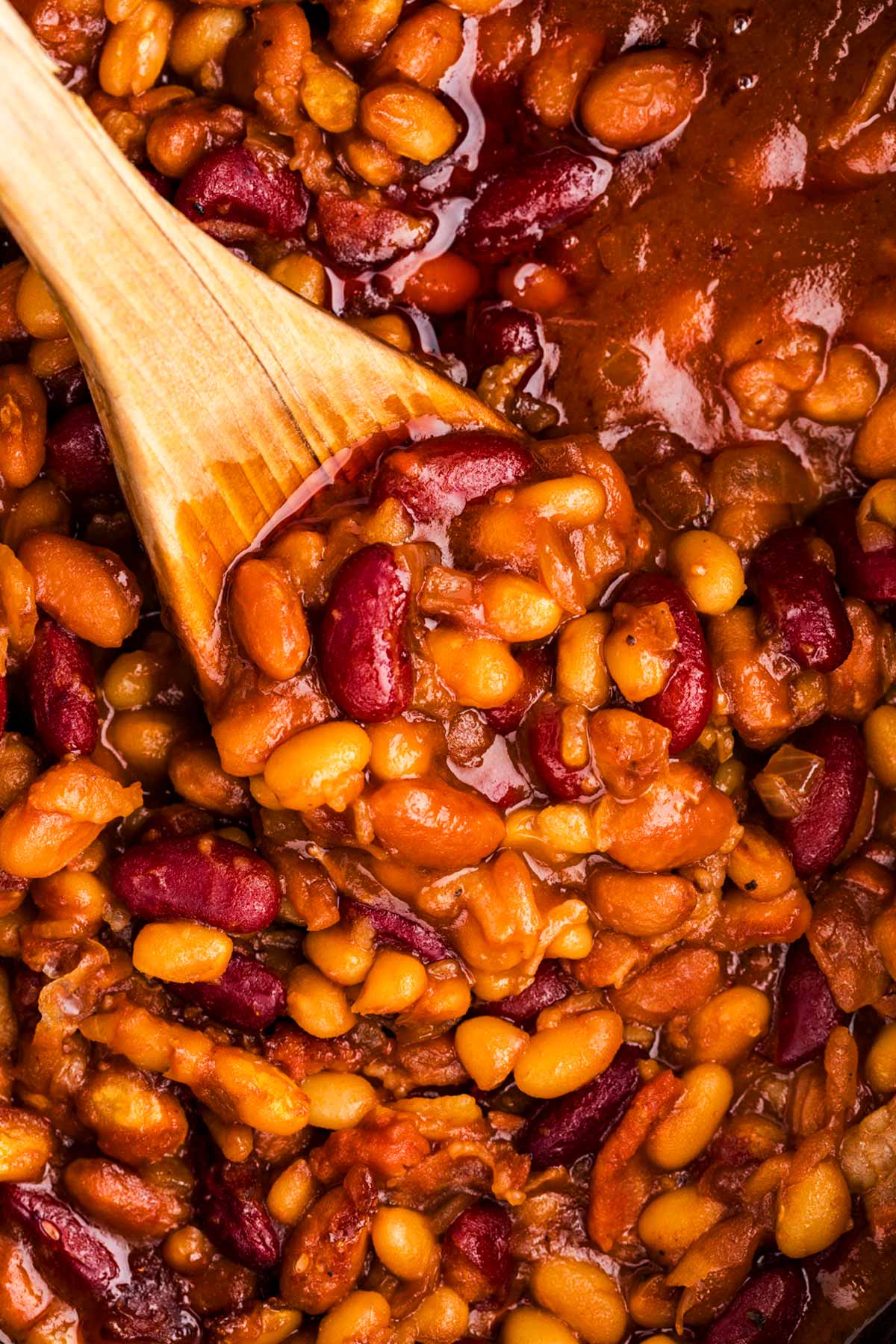 Close up photo of a wooden spoon in a slow cooker full of baked beans.