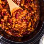 Overhead view of a wooden spoon in a crockpot full of baked beans.