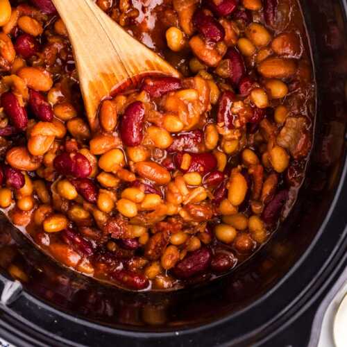 Overhead view of a wooden spoon in a crockpot full of baked beans.