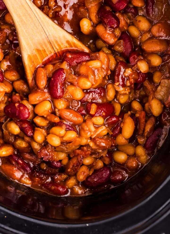 Overhead view of a wooden spoon in a crockpot full of baked beans.