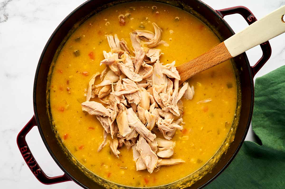 Adding pulled chicken to a pot with corn chowder.