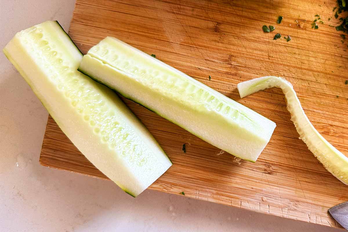 Seeded cucumber quarters on a wooden cutting board.