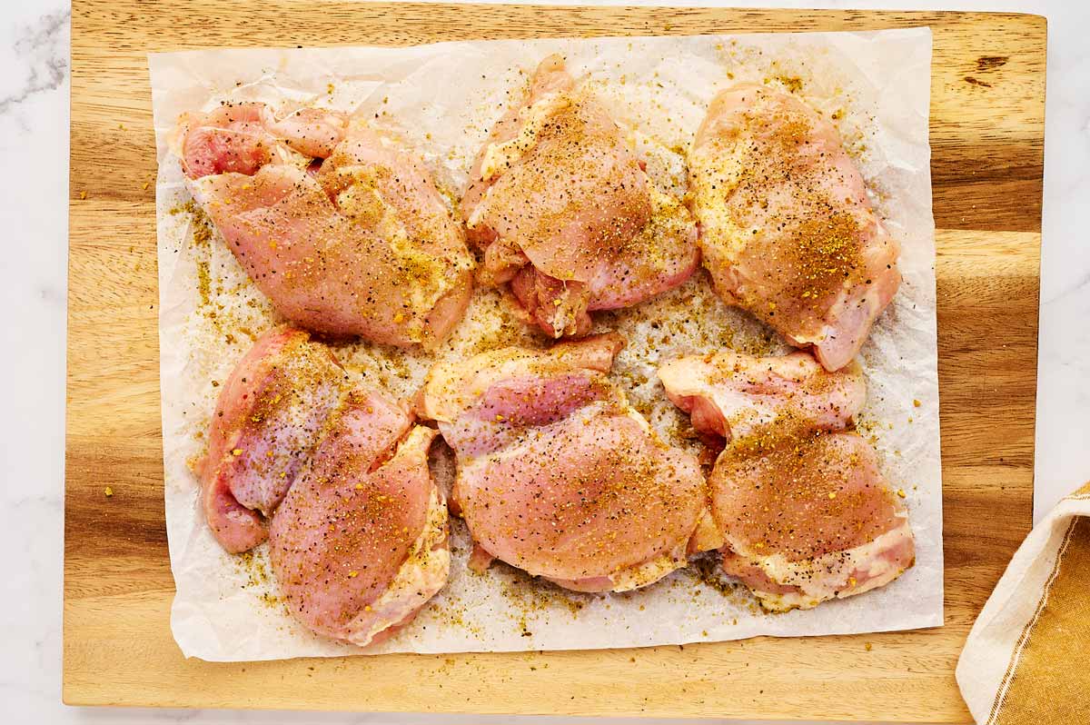 Seasoned chicken thighs on wooden board.
