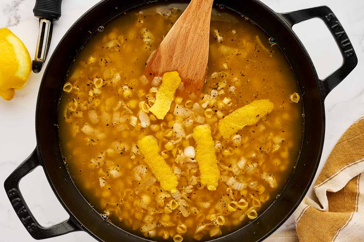 Strips of lemon zest in a skillet with broth and onion.