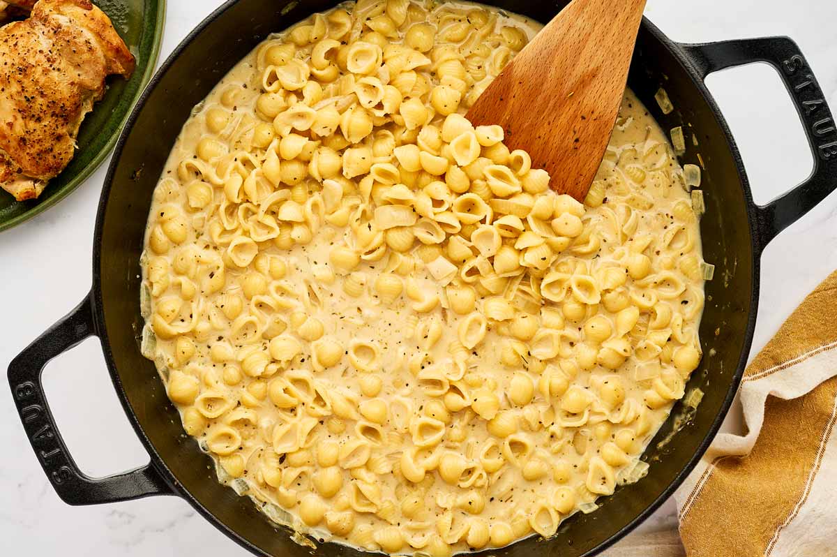 Stirring creamy pasta in a cast iron skillet.