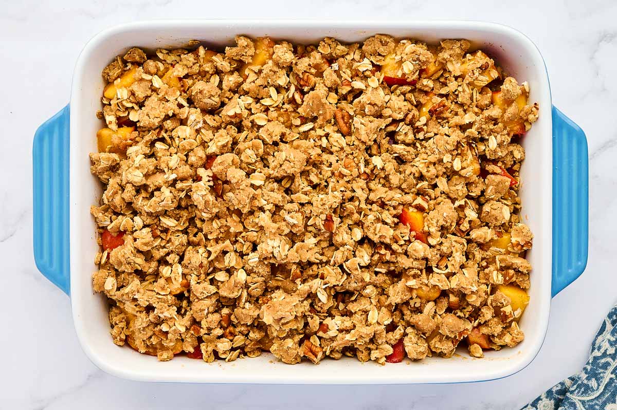 Unbaked peach crisp in a blue casserole dish.