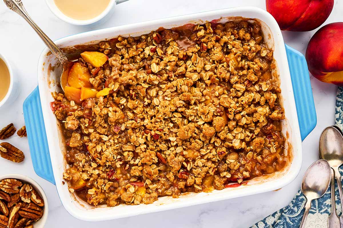 Serving peach crisp from a blue casserole dish.