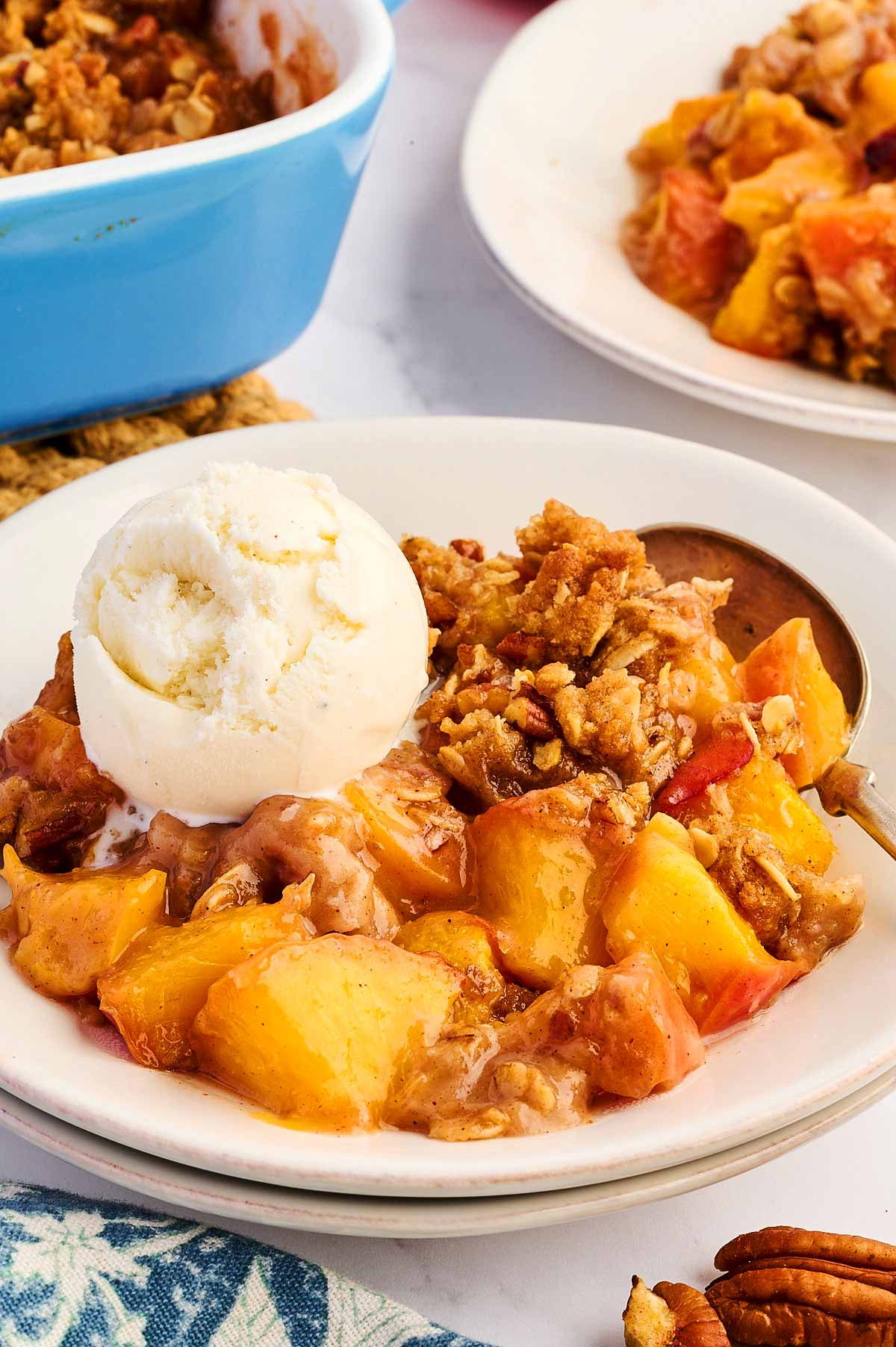 Frontal closeup of peach crisp in a bowl with a scoop of vanilla ice cream.