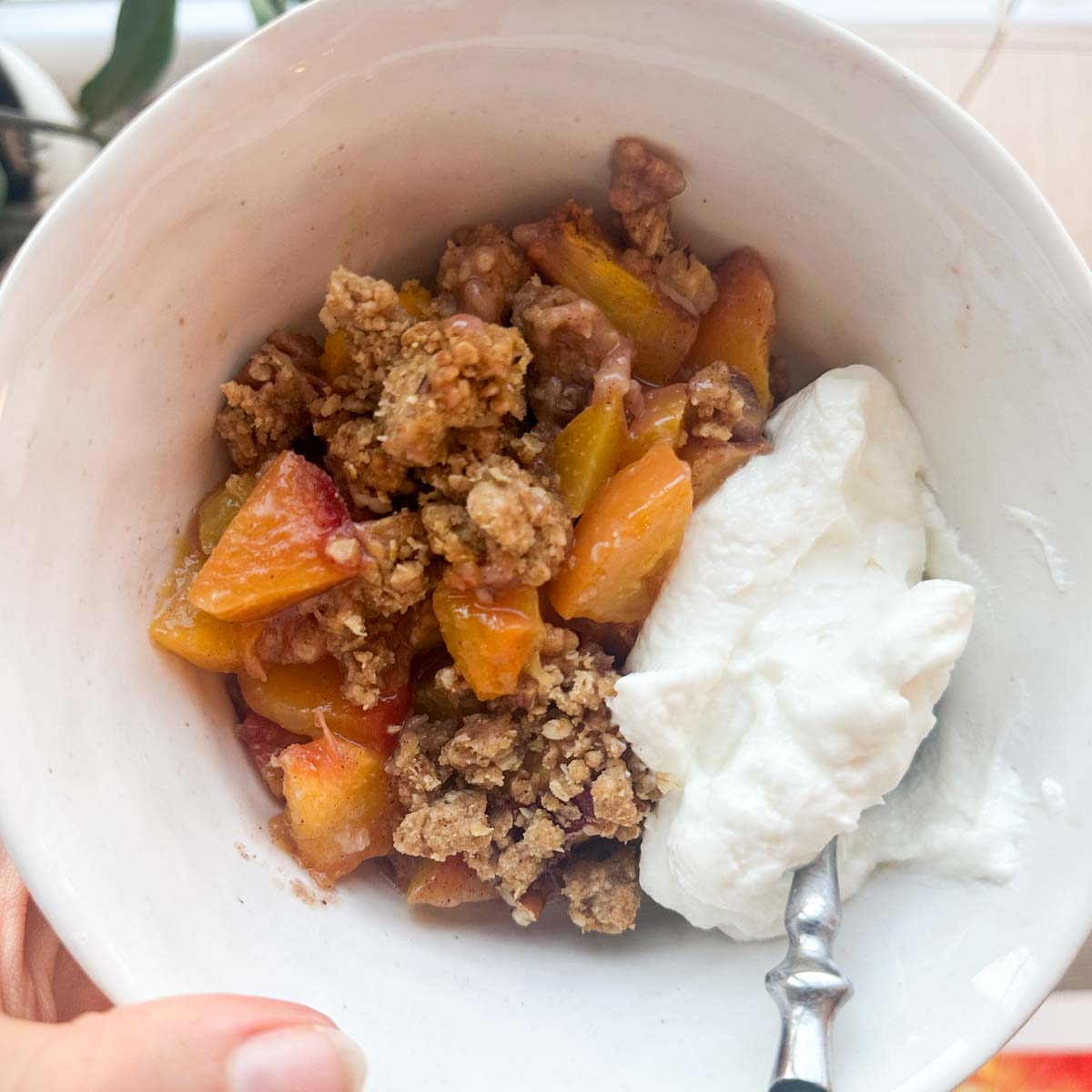 Female hand holding a white bowl with peach crisp.