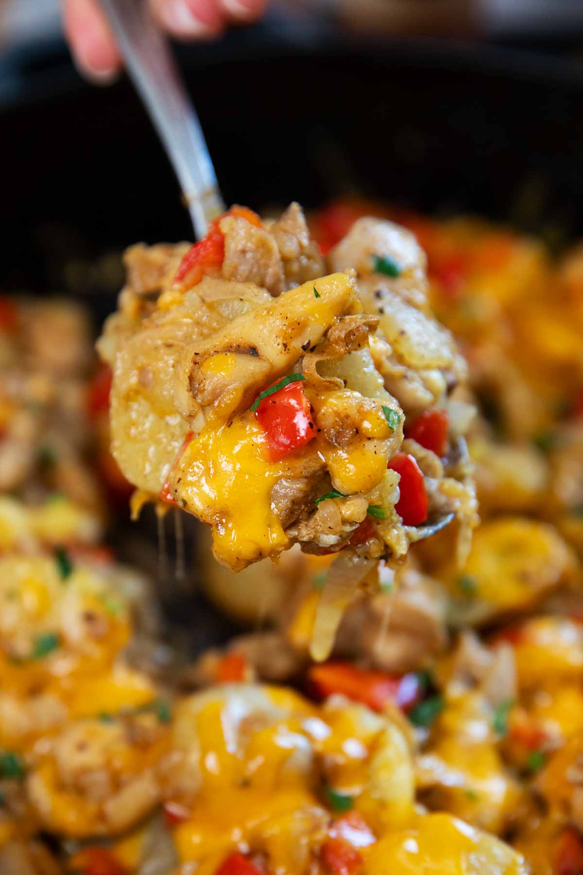Close up of a spoon scooping chicken and potatoes.
