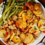 Plate with green beans, cajun chicken and potatoes and buttered bread on the side.