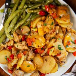 Plate with green beans, cajun chicken and potatoes and buttered bread on the side.