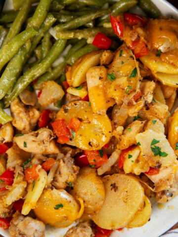 Plate with green beans, cajun chicken and potatoes and buttered bread on the side.