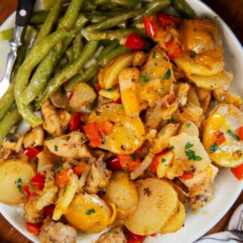 Plate with green beans, cajun chicken and potatoes and buttered bread on the side.