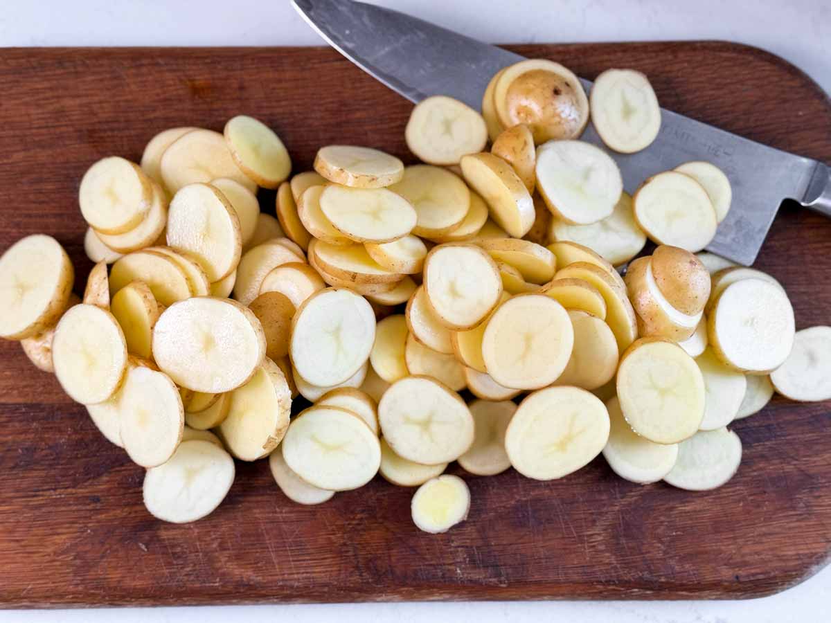 Thinly sliced potatoes on a wooden cutting board.