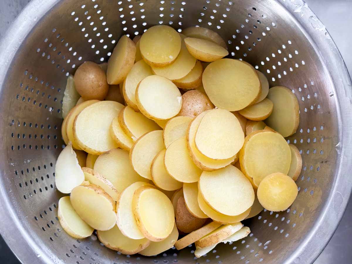 Cooked potato slices in colander.