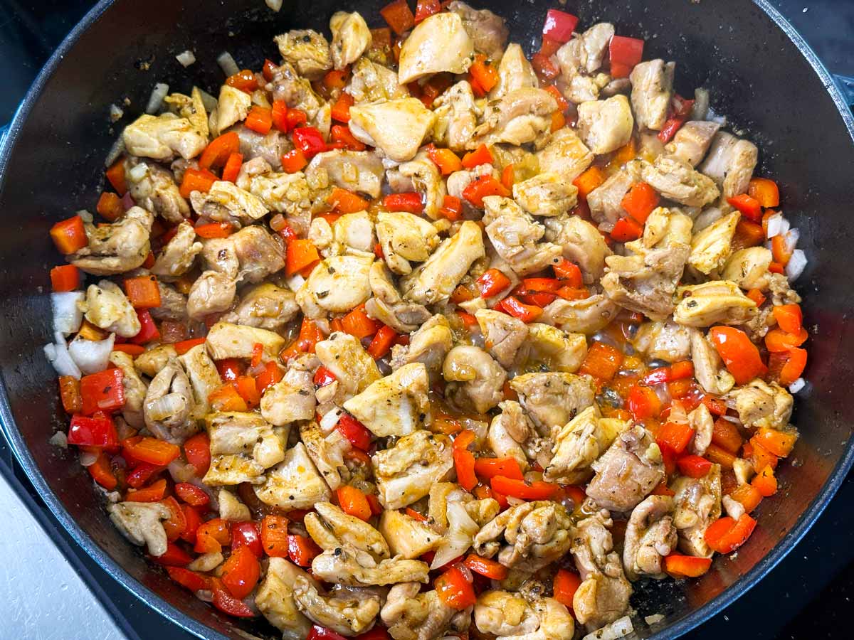 Chicken pieces, diced onion and diced bell pepper cooking in a cast iron skillet.