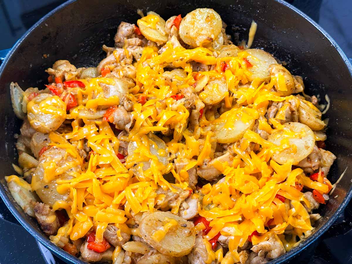 Cheese on top of cajun chicken and potatoes in a skillet.