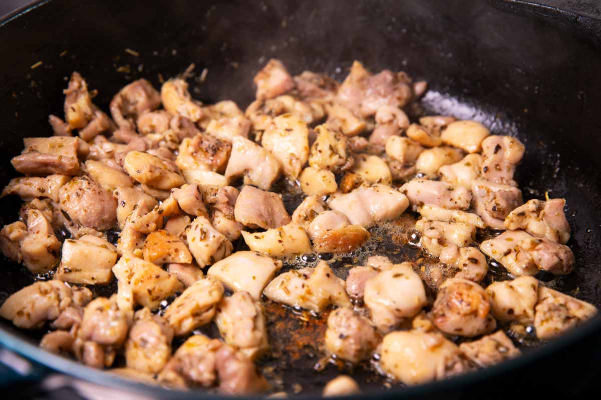 Browned bite-sized chicken thighs in a cast iron skillet.