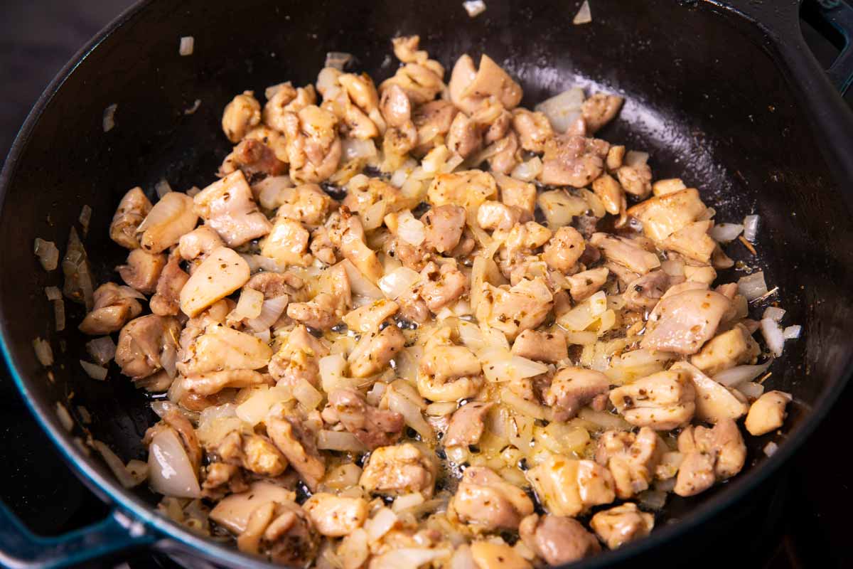 Browned bite-sized chicken thighs and chopped onion in a cast iron skillet.