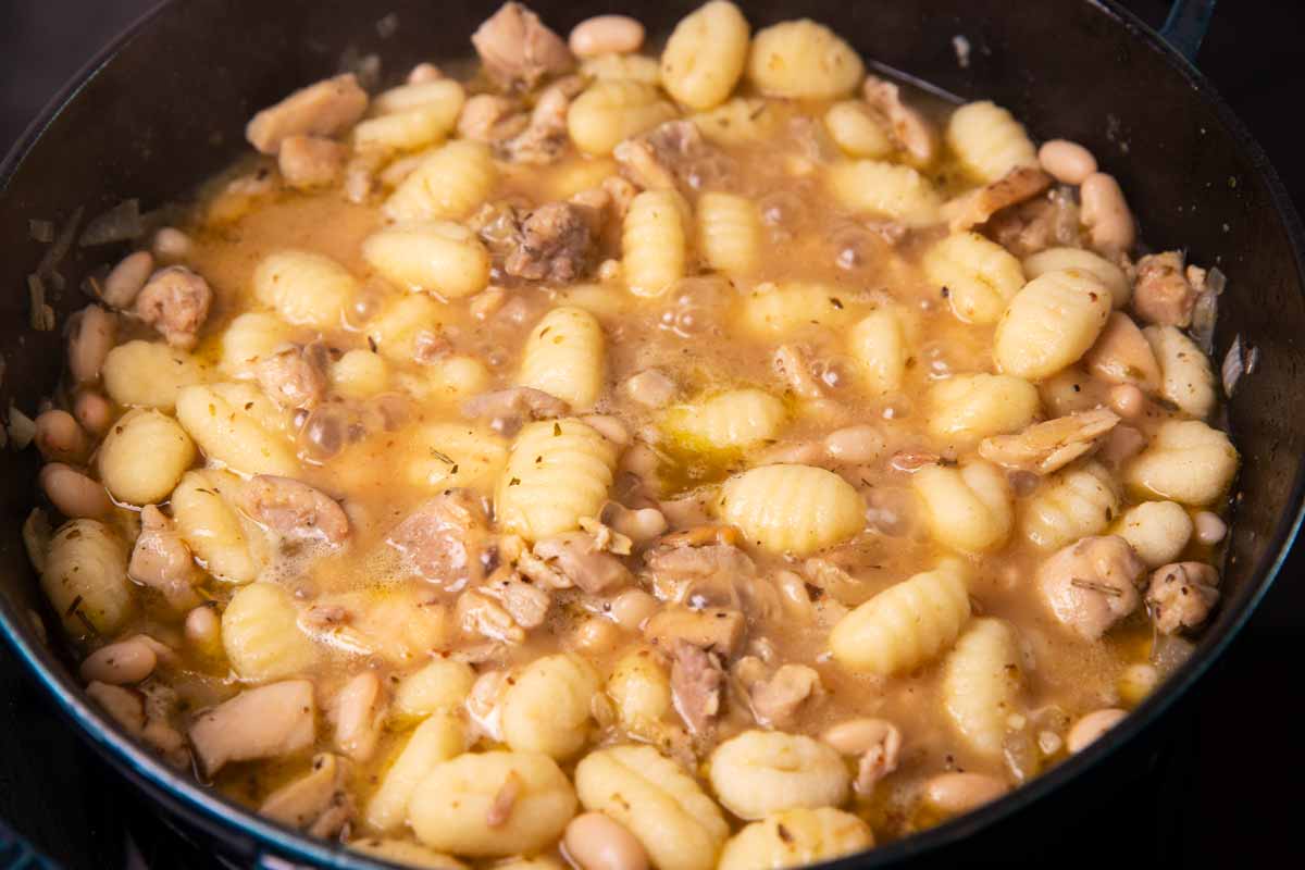 Chicken, gnocchi and white beans simmering in broth in a cast iron skillet.
