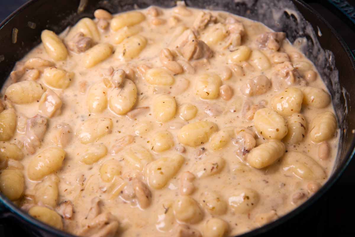 Creamy sauce with chicken, gnocchi and white beans in a cast iron skillet.