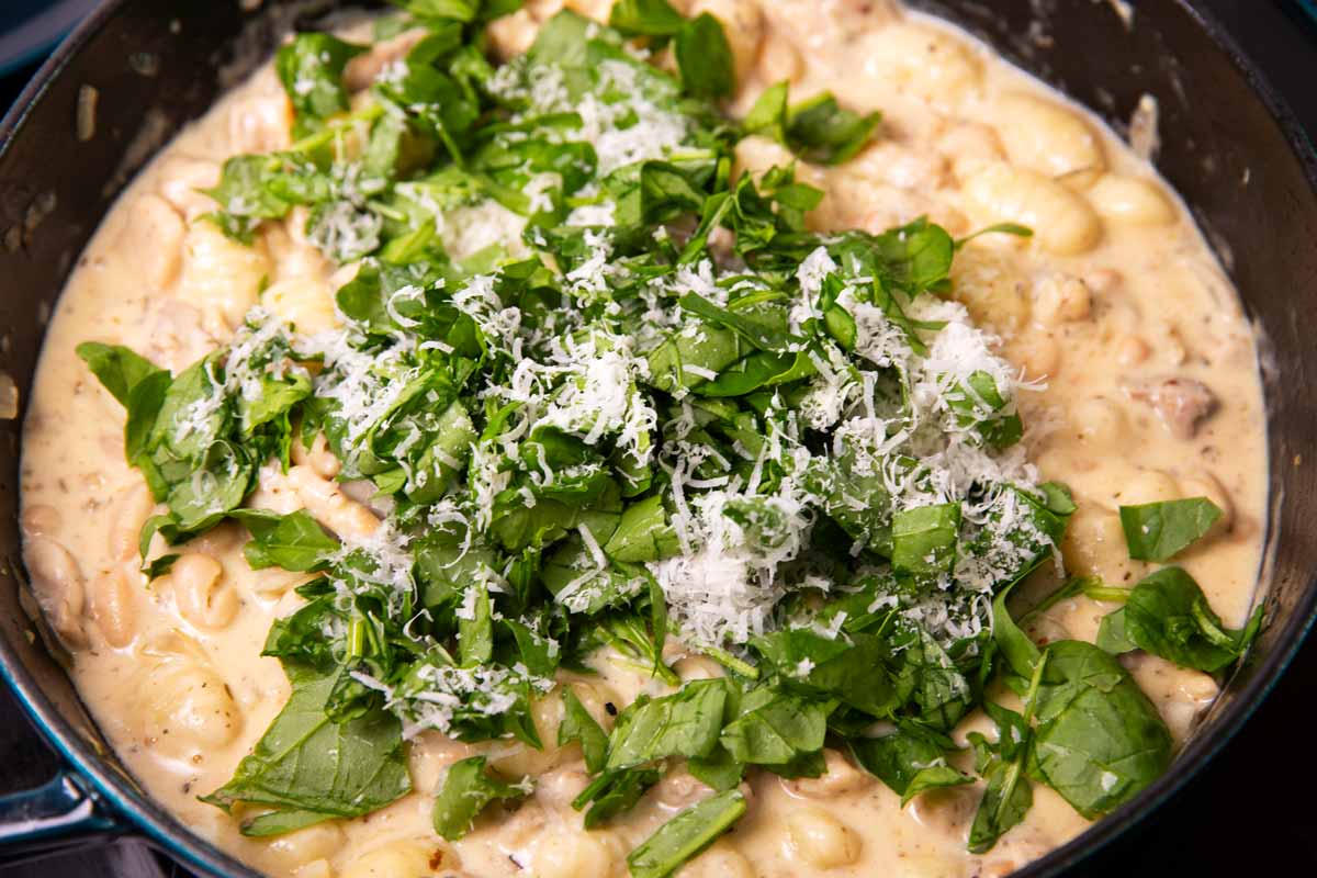 Chopped fresh baby spinach and grated parmesan cheese on top of creamy chicken gnocchi in a cast iron skillet.