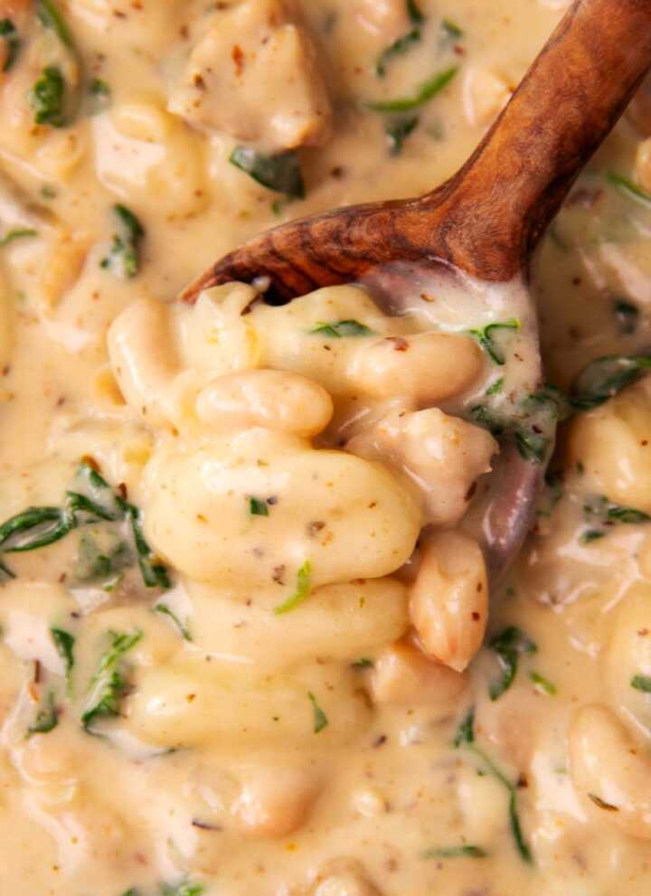 Close up photo of a wooden spoon scooping up creamy chicken and gnocchi.