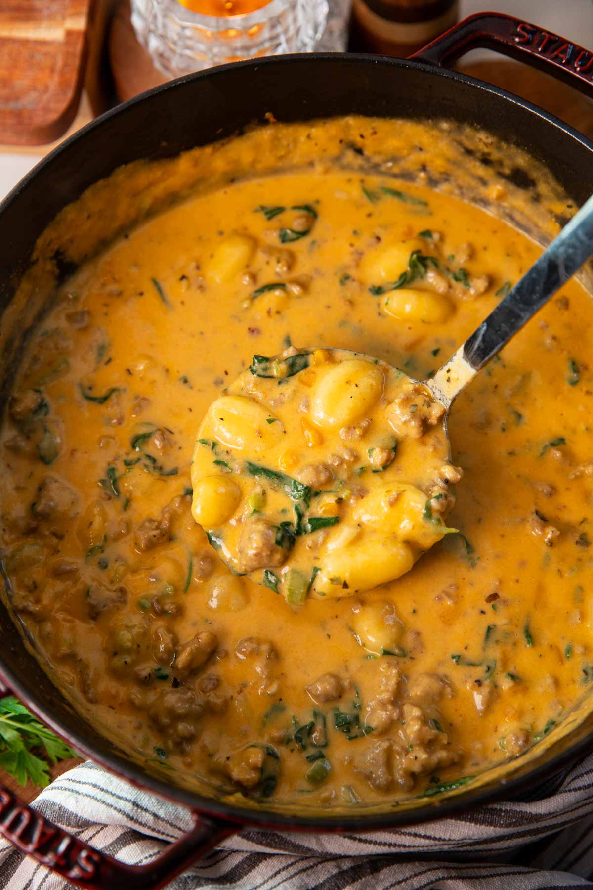 Overhead view of a soup ladle removing sausage gnocchi soup from a cast iron pot.