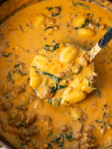 Overhead view of a soup ladle removing sausage gnocchi soup from a cast iron pot.