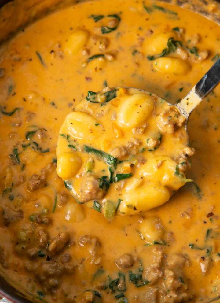 Overhead view of a soup ladle removing sausage gnocchi soup from a cast iron pot.