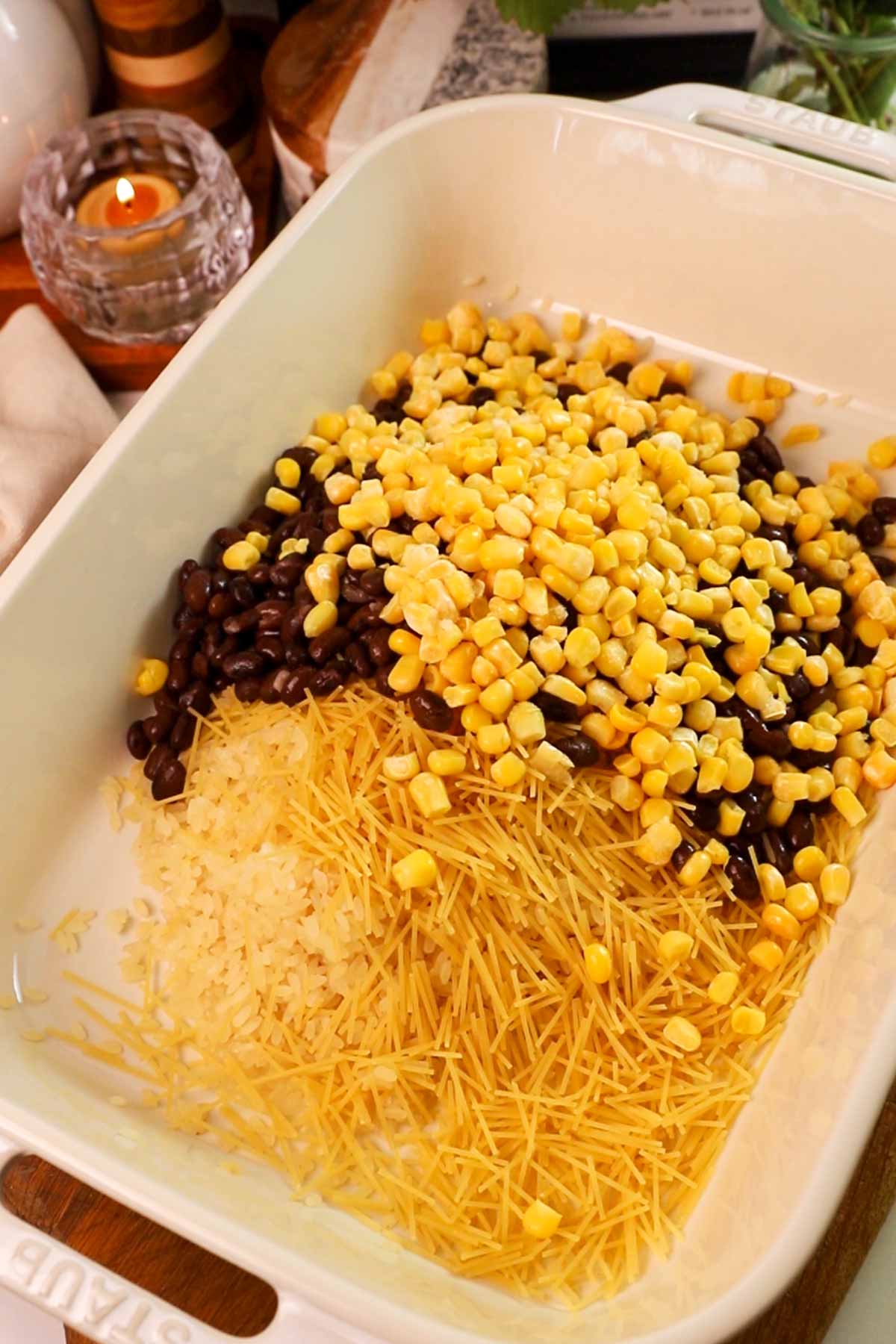 Uncooked rice, beans and corn in a casserole dish.