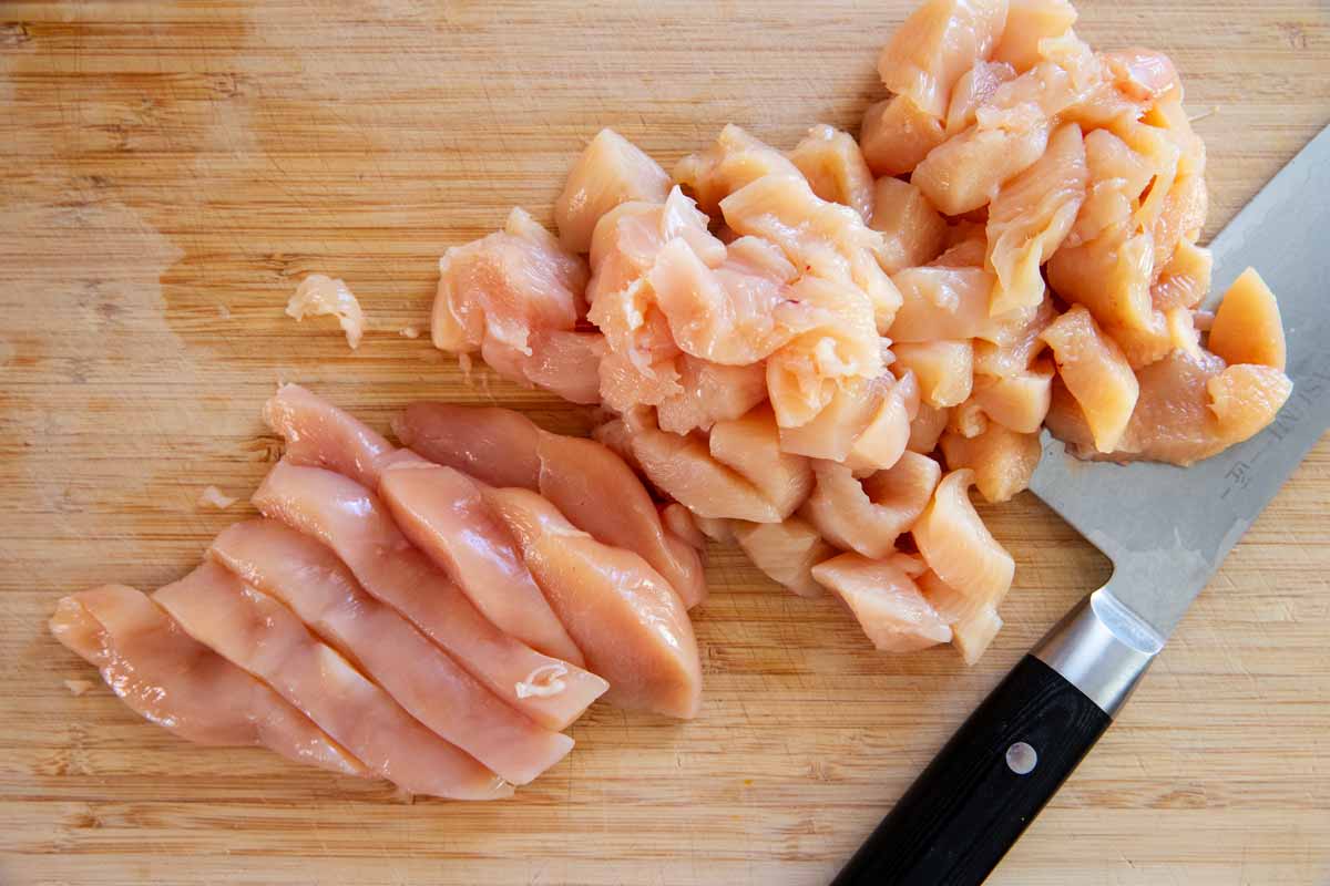 Cut up chicken breast on a wooden cutting board.