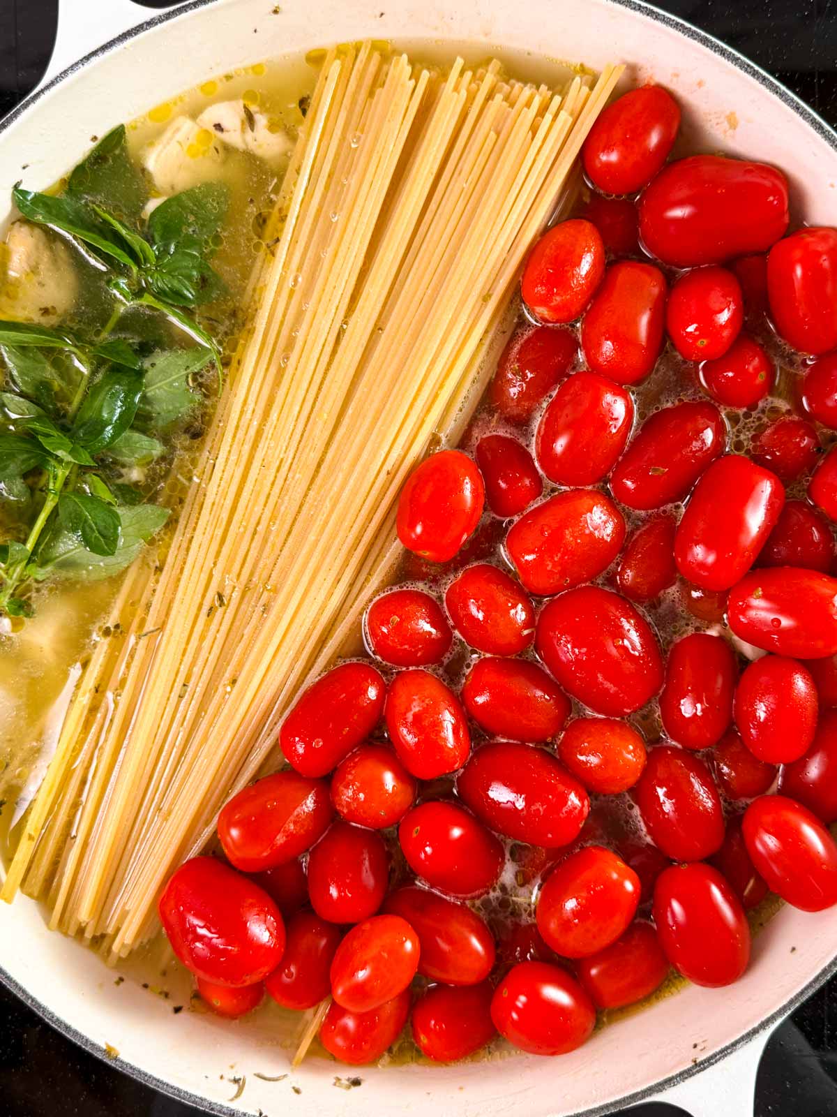 Uncooked spaghetti, grape tomatoes and basil in skillet.