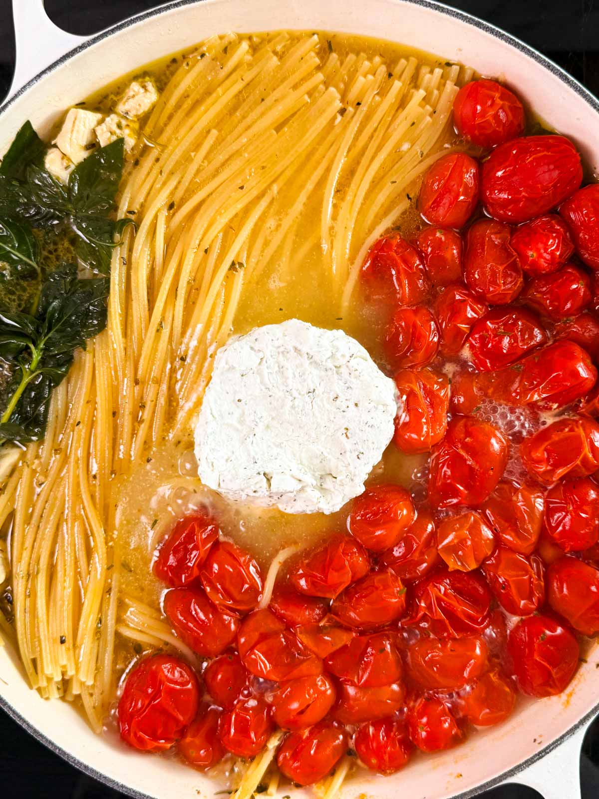 Garlic herb cheese in a pan with cooked spaghetti, grape tomatoes and basil.
