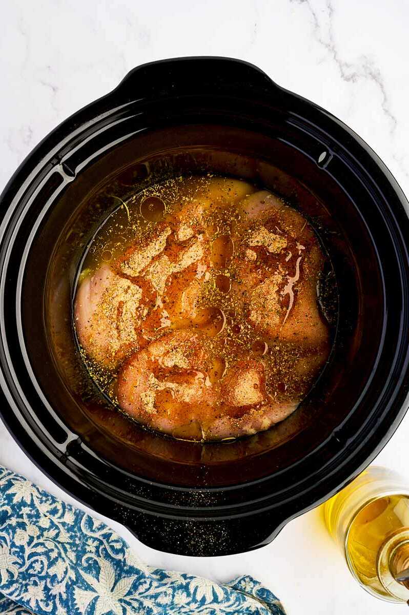 Raw chicken breast in a crockpot with seasoning.